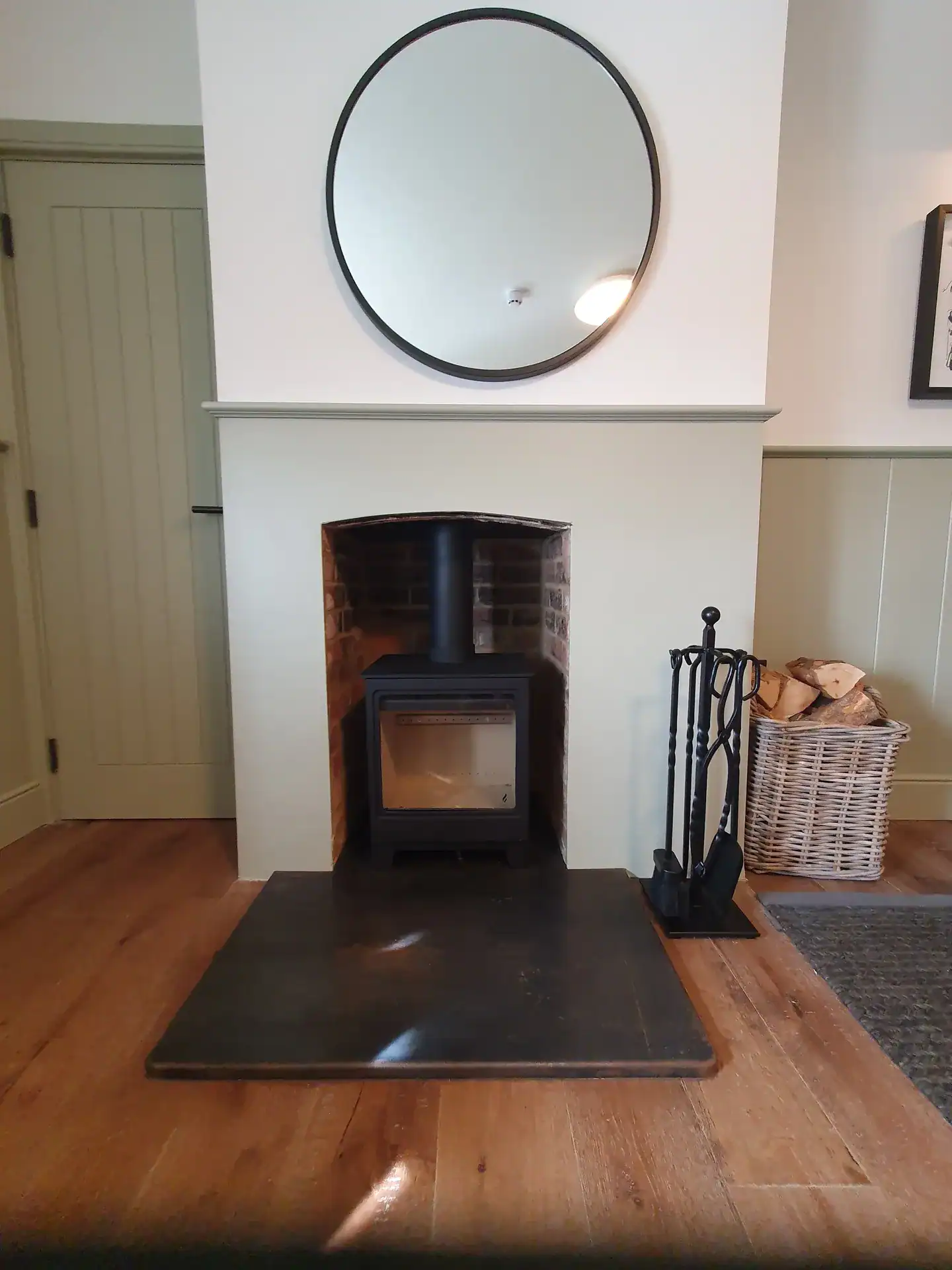 Modern fireplace with wood storage and round mirror in a stylish living room.
